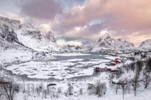 Snow-covered mountains and frozen lake under a pastel winter sky, capturing the serene beauty of Iceland winter magic in a charming village setting.