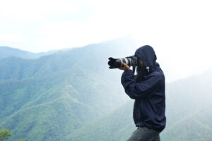 "A photographer in a hooded jacket capturing scenic mountain landscapes with a professional camera, showcasing nature as the foundation of life and well-being