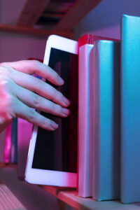 Hand holding a tablet for Digital Reading beside a collection of books.