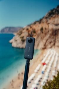 Insta360 camera mounted on a selfie stick overlooking a scenic beach and rocky coastline.