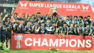 Football team celebrating with a silver trophy on stage at the Super League Kerala Season 01 final, standing behind a red "Champions" banner.