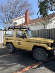 toyota Landcruiser parked in front of a house with a roof rack and off-road tires.
