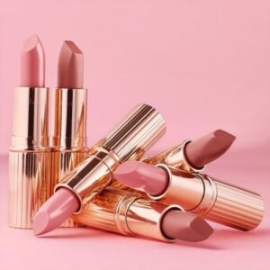 Best lipsticks shades in pink and nude tones displayed in elegant rose-gold tubes on a pink background.