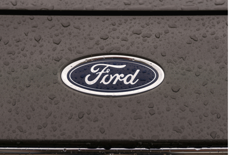 Close-up view of a Ford car logo on a wet hood, with raindrops covering the surface. Close-up view of a Ford car logo on a wet hood, with raindrops covering the surface.