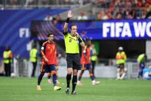 A referee signals a VAR review during a FIFA World Cup match, highlighting the use of video technology in modern football.
